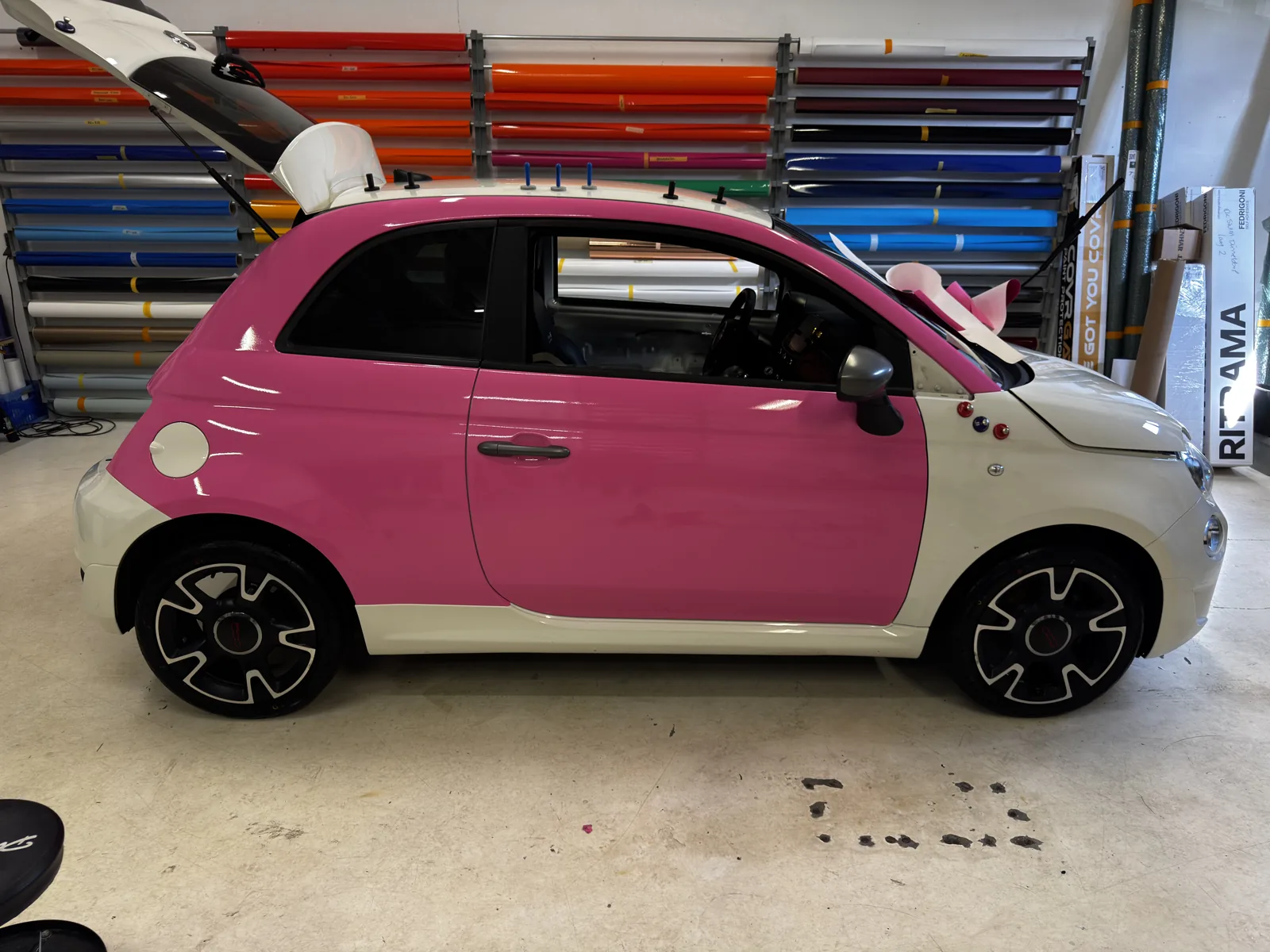 Roze wrapfolie wordt aangebracht op een compacte auto in de werkplaats